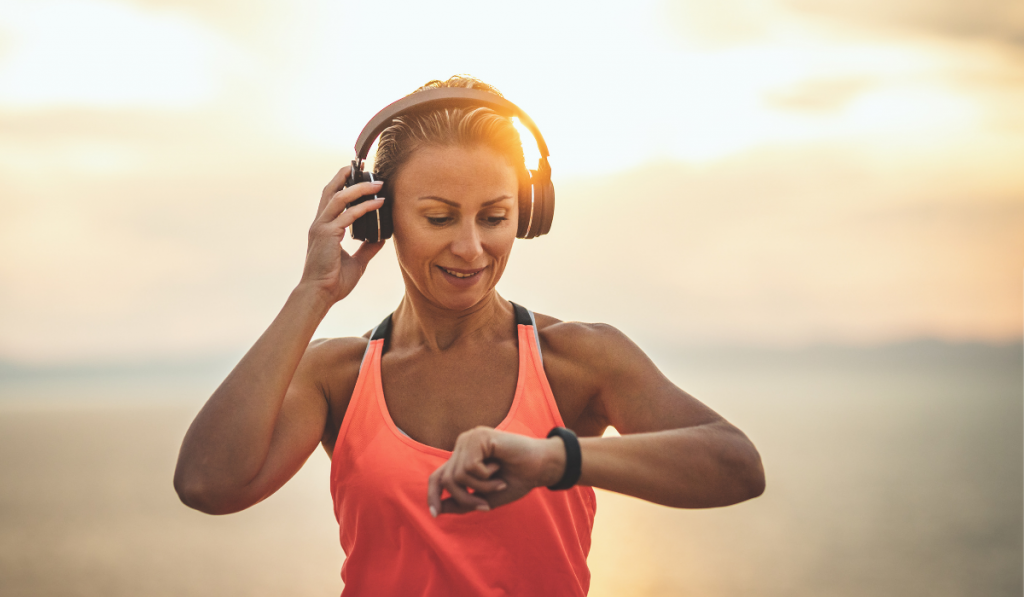 A beautiful young woman is ready to do stretching exercise by the sea in sunrise hearing music by headphones.