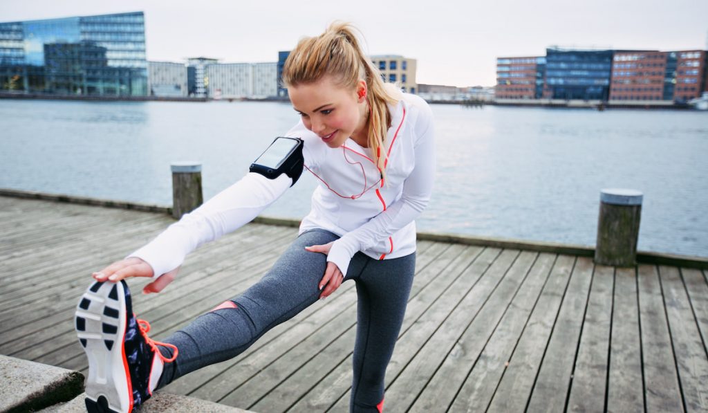 Female runner stretching before a run near river 