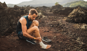 Male-runner-bandaging-injured-ankle.-Injury-leg-while-running-outdoors