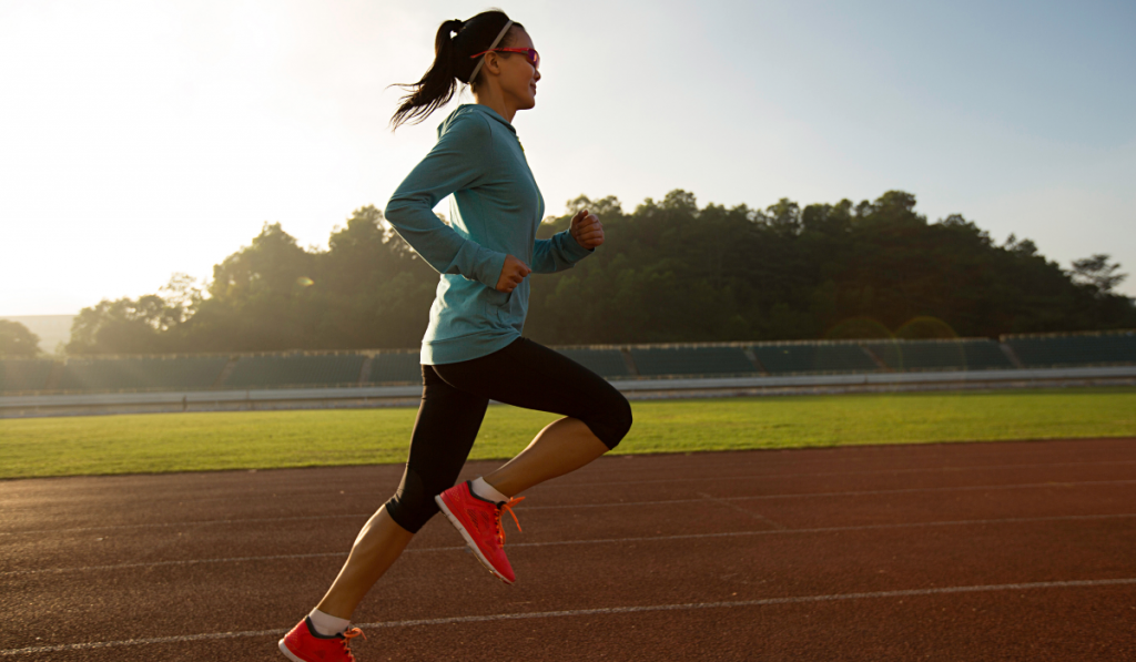 Young woman running during sunny morning on stadium track