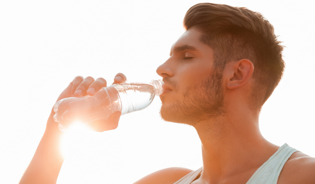 Staying hydrated. Low angle view of young man drinking water and keeping eyes closed while standing outdoors
