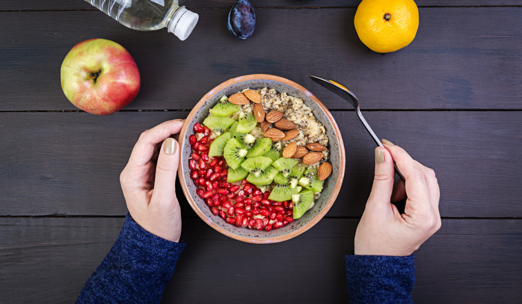 top view of a woman holding a healthy bowl for breakfast with some apple, orange and a bottle of water on the table