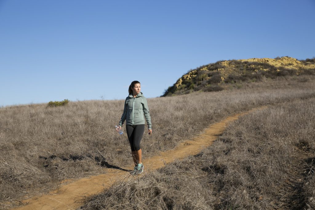 female holding a bottle of water walking on a downhill 