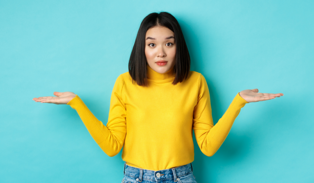 Image of indecisive asian woman shrugging shoulders, spread hands sideways and looking clueless at