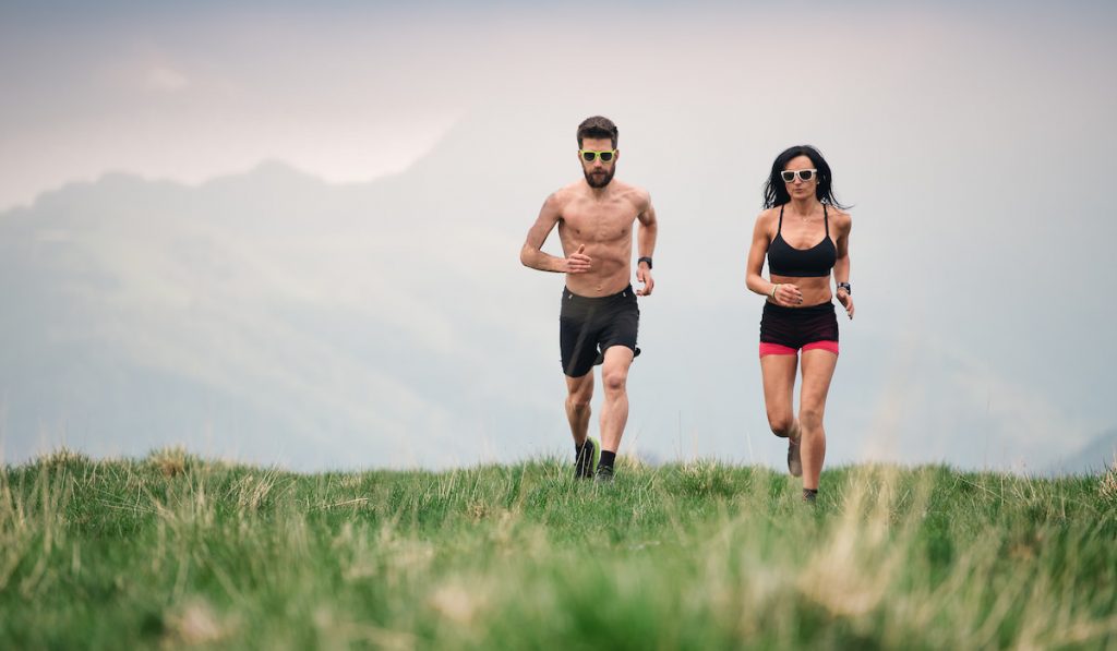 sporty man and woman running together  grass field 
