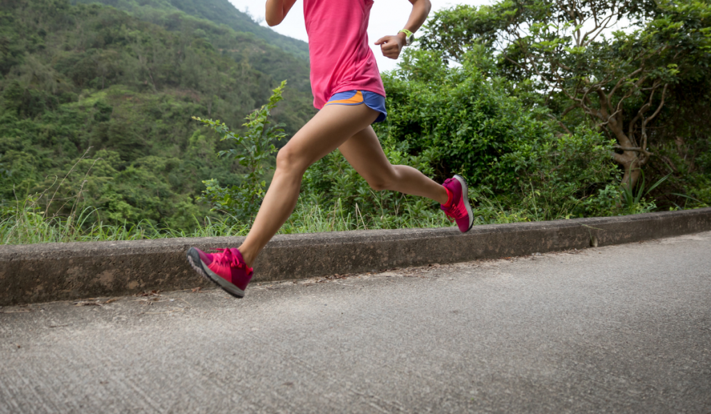 Sporty young woman in sportswear trail running on forest mountain path.