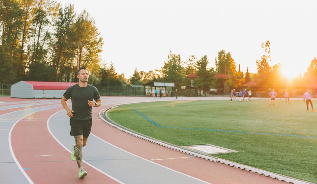 young athletic fit man running on track sunset