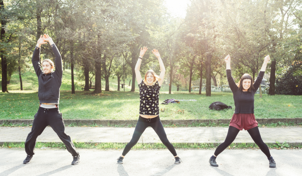 young woman and men doing jumping jacks outdoors
