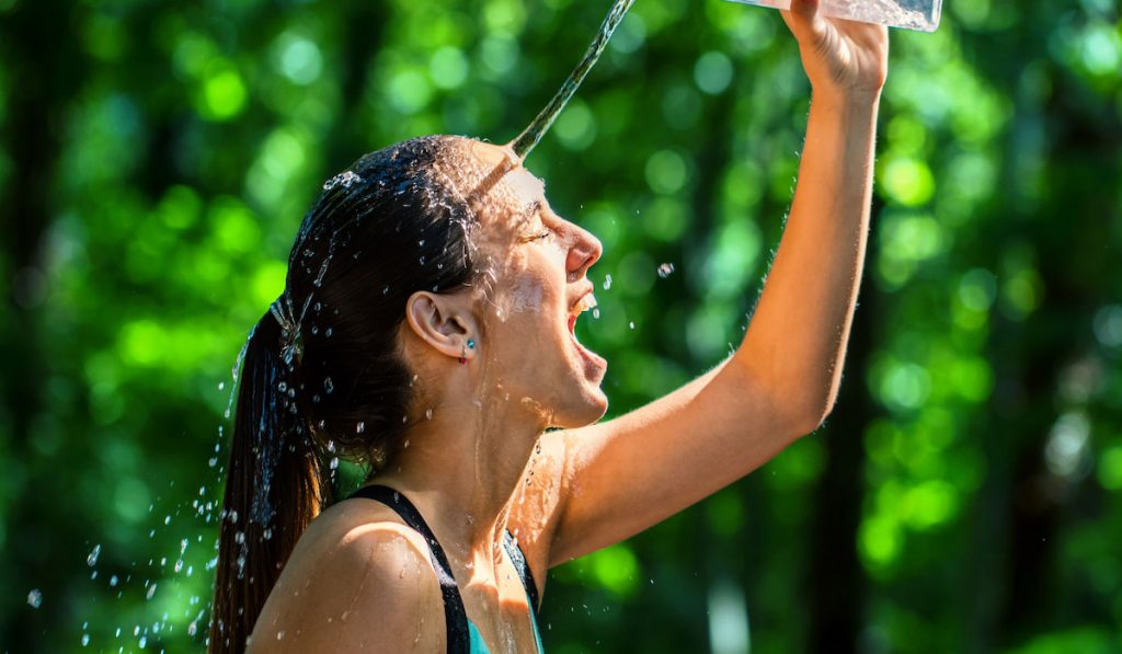 female runner pouring water on her face after running