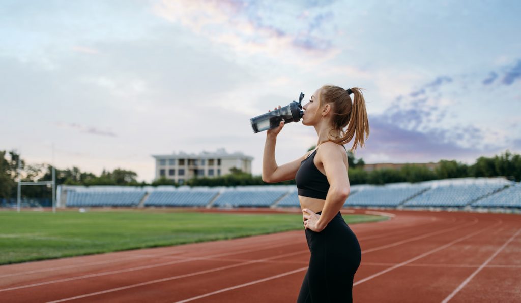 Female runner drinks water, training on stadium
